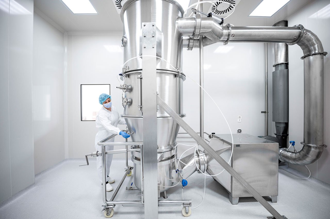 Woman wearing protective wear seen working on the machine in a laboratory during pharmaceutical manufacturing
